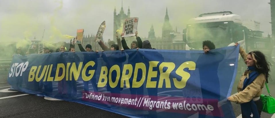 Protesters hold banner reading Stop Building Borders