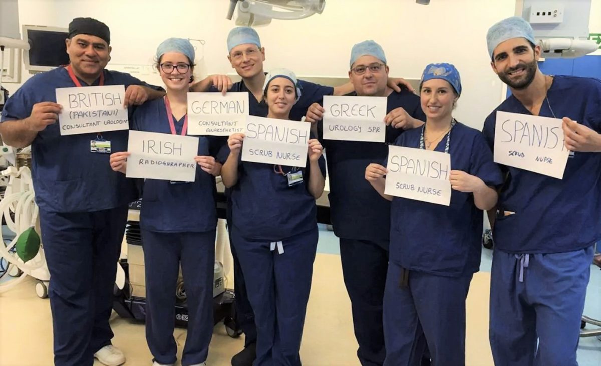 A team of NHS workers in scrubs hold signs declaring the different countries they come from.